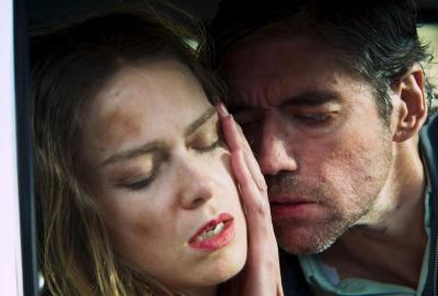A dramatic close-up of a man with short facial hair gently caressing the face of a woman with her eyes closed, leaning in closely to her.