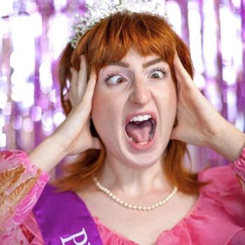 A young woman with red hair wearing a prom dress, crown, and sash is screaming comedically.